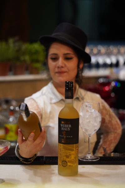 Bartender Jocassia Coelho contemplando uma garrafa de Weber Haus 7 Madeiras, Capitão Leitão, Belo Horizonte